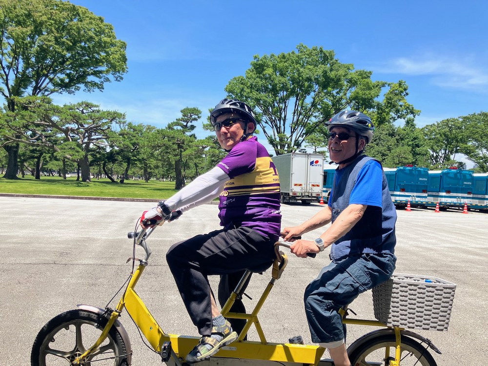 公園の広場で二人がタンデム自転車に乗っている様子