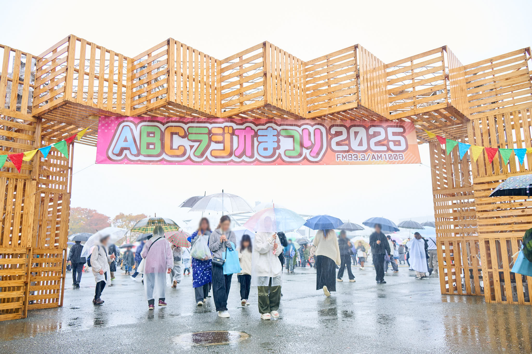 ABCラジオまつり2025の入口ゲート、雨の中で傘を差して歩く来場者