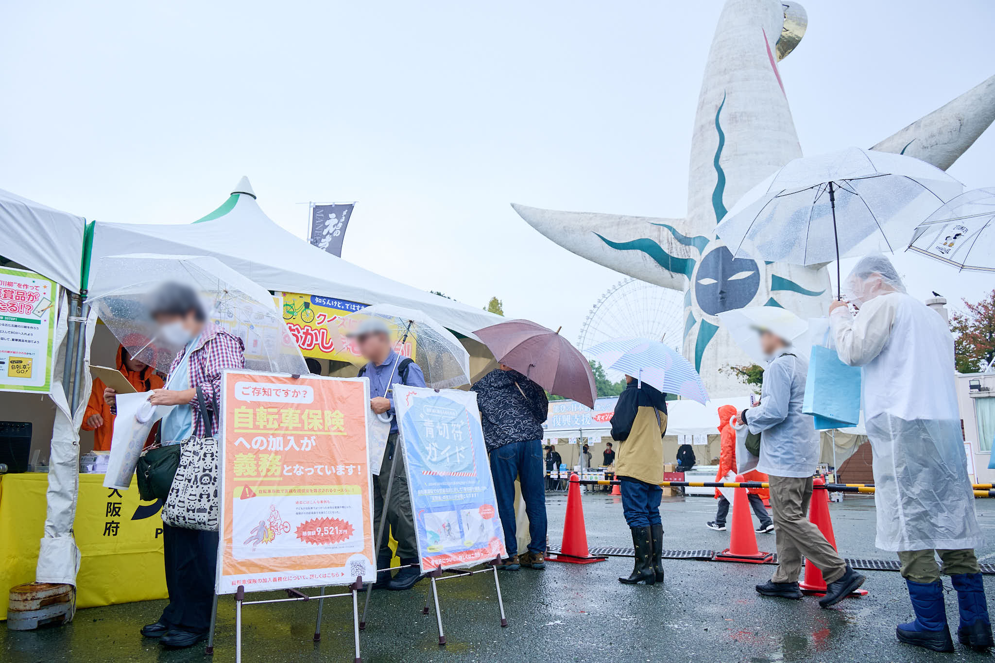 太陽の塔前のイベント会場、雨の中で傘を差しながらテントに並ぶ来場者