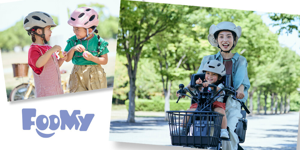 屋外の緑豊かな並木道で、大人が自転車に乗り前カゴに子どもを乗せて走っている様子と、別の場面で子ども用ヘルメットを着用した2人の子どもが立ち話をしている様子。背景には自転車や木々があり、明るい自然光が差し込む公園の雰囲気。画像下部に『FooMy』のロゴが表示されている。