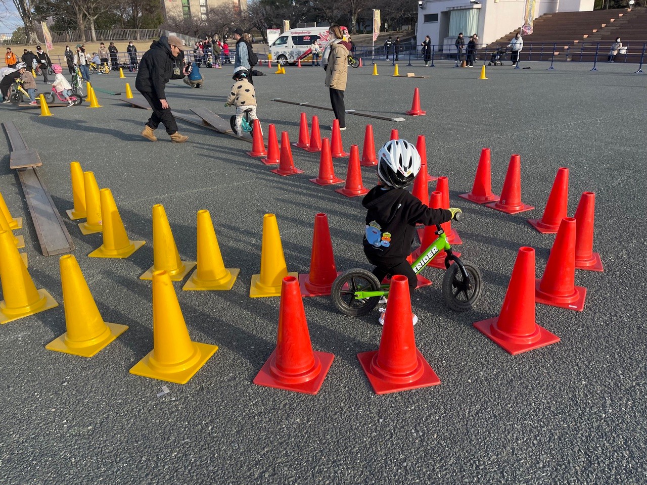 カラーコーンで作られたコースを、子どもがヘルメットを着用してストライダーで走行している様子。