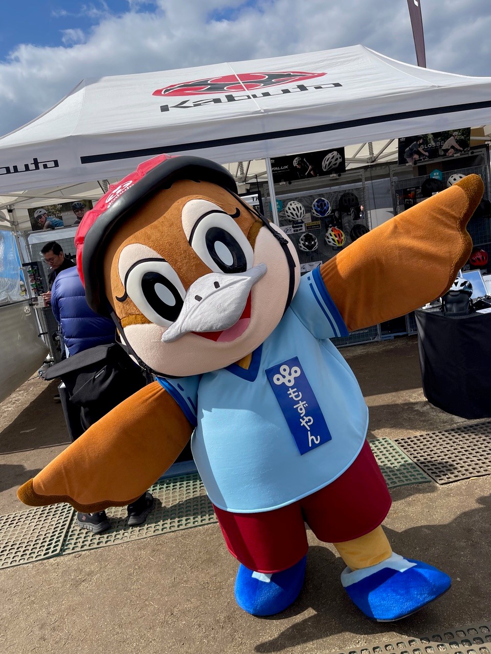 展示ブース前で、自転車ヘルメットを着用したマスコットキャラクター(もずやん)がポーズをとっている様子。