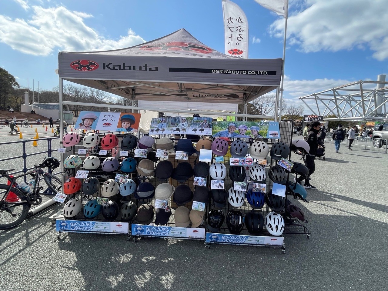 自転車用ヘルメットが多数並んだ展示ラックと、OGK Kabutoのテントが設置されたヘルメット販売ブース。